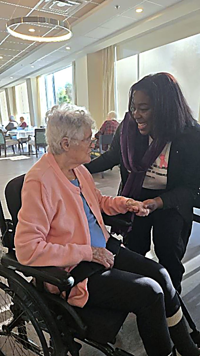 Yvette pench&eacute;e vers une a&icirc;n&eacute;e en fauteuil roulant, lui tenant la main en souriant